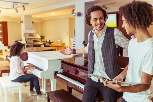 A woman plays a piano while two other people shop for a piano.